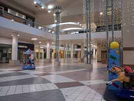 A photo of the center court of the Crossroads Mall, looking southwest from the east court. Visible are storefronts in the east and west courts, all empty.