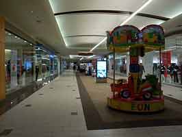 The south hall of the Empire Mall. Open storefronts are to the left and right, with a kids carousel and directory in the middle of the corridor.